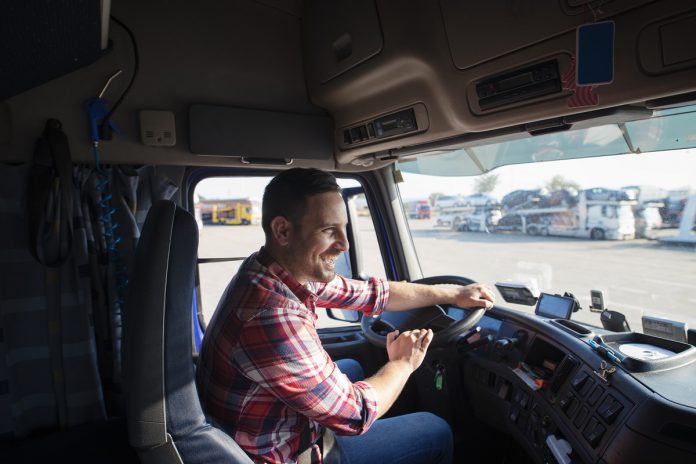 Professional truck driver with smile driving truck and delivering goods on time. Fast transportation service.